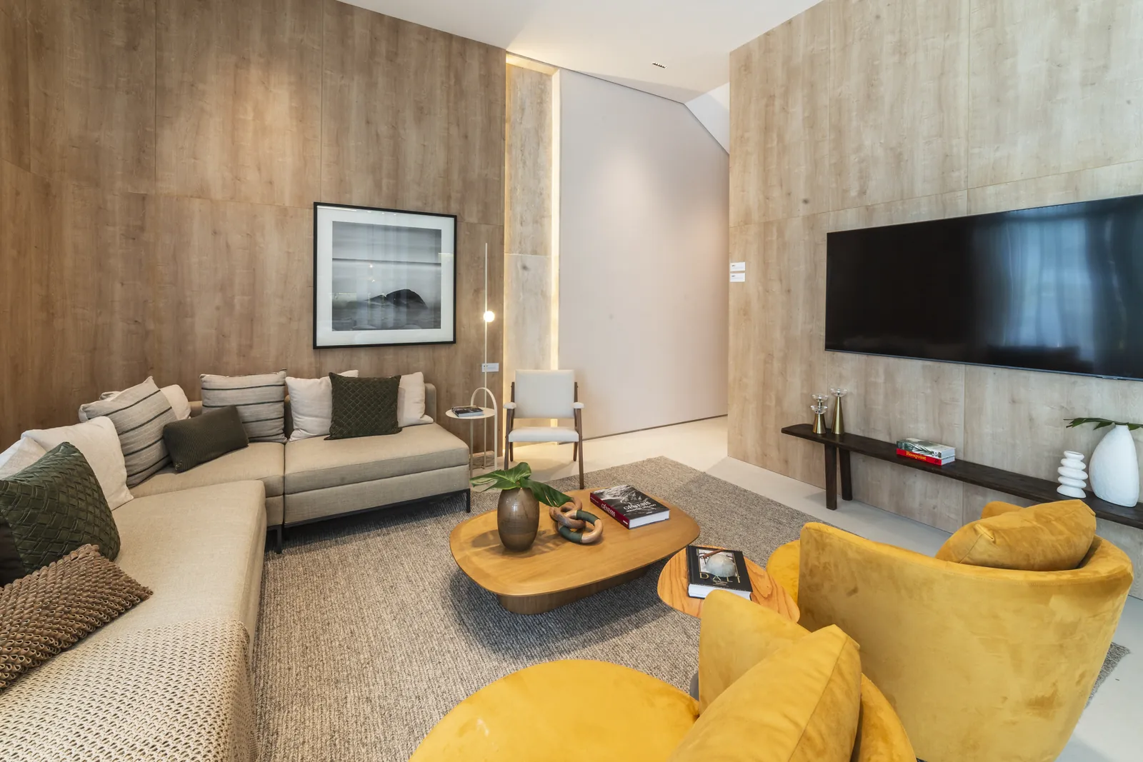 Sala do decorado com poltronas amarelas, sofá e painel de madeira