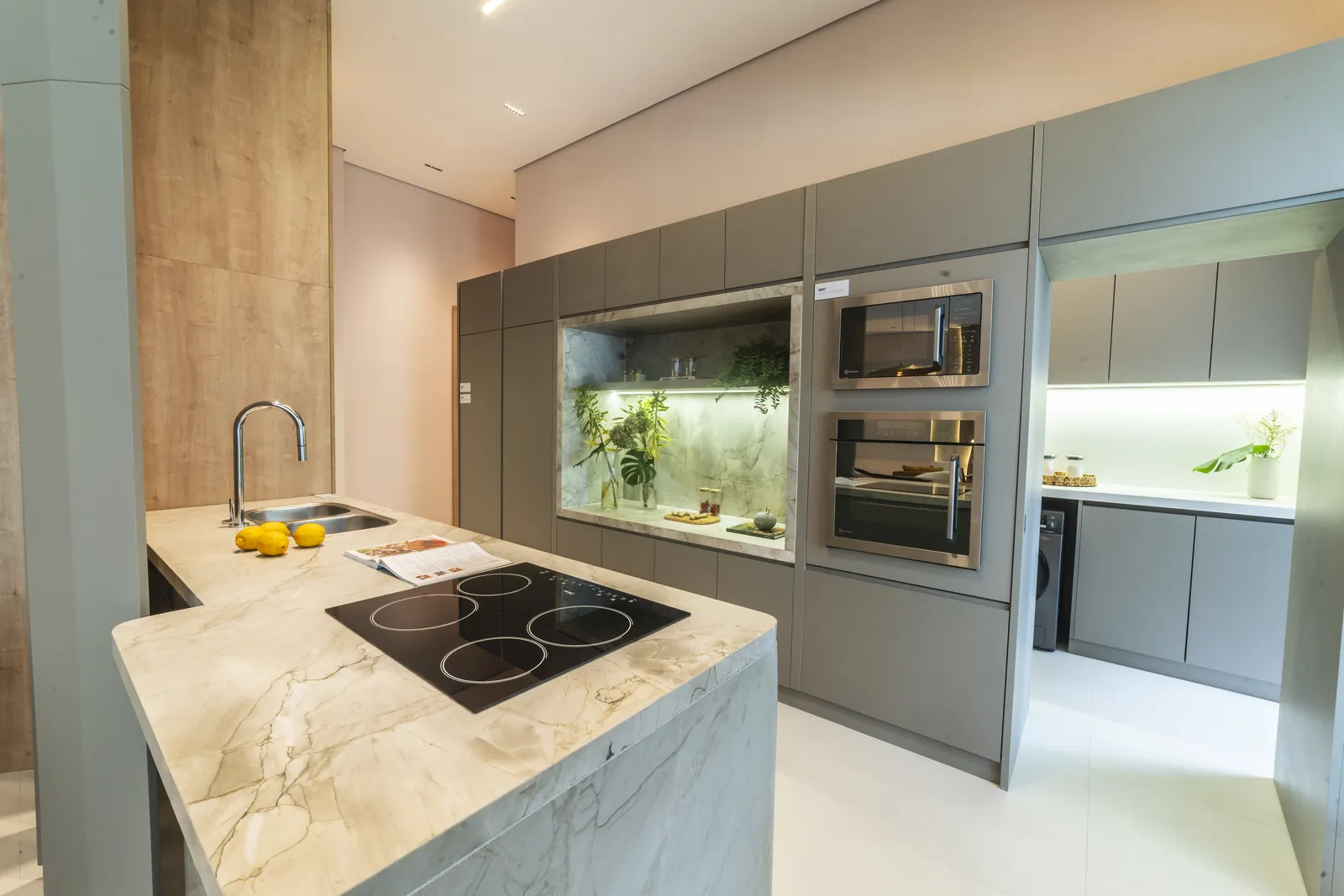 Cozinha com ilha de pedra clara, cooktop e armários escuros