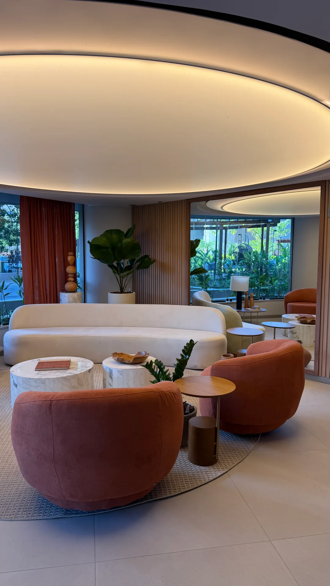 Lobby com forro curvo iluminado, sofá orgânico e poltronas terracota